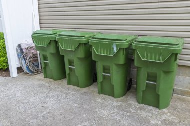Dört yeşil plastik çöp tenekesinin yatay görüntüsü bir apartmanın dış duvarına karşı dizilmiş..