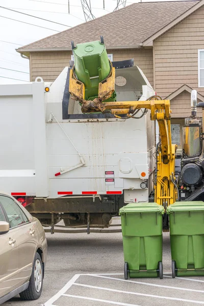 Vertical shot of a garbage truck with a robot arm dumping trash from a residential trash container.