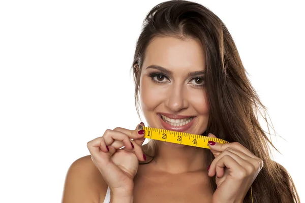 Smiling young woman holding measuring tape under her mouth — Stock Photo, Image