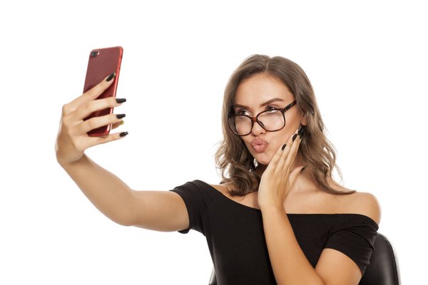 Young woman with eyeglasses making selfie on a white background