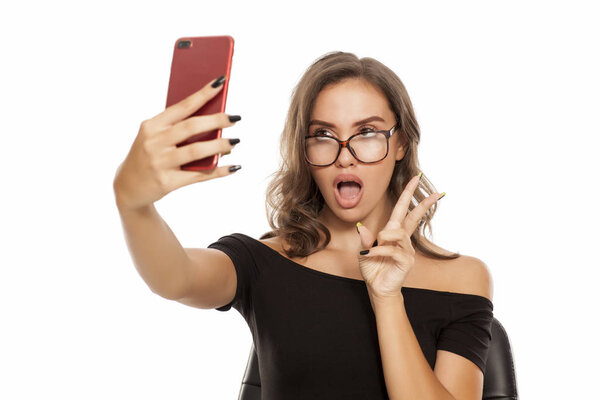 Young woman with eyeglasses making selfie on a white background