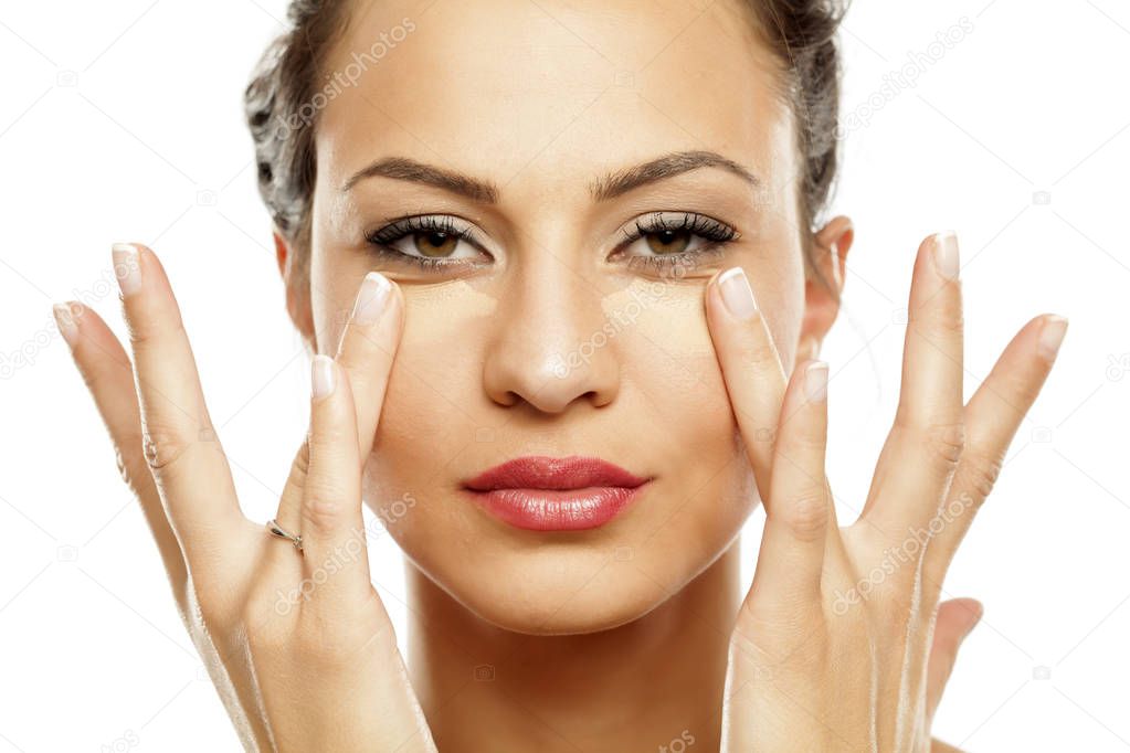 Young beautiful woman applying concealer under her eyes with her fingers