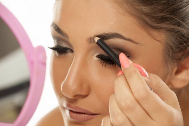 Young woman shaping her eyebrows with an eyebrow pencil clipart