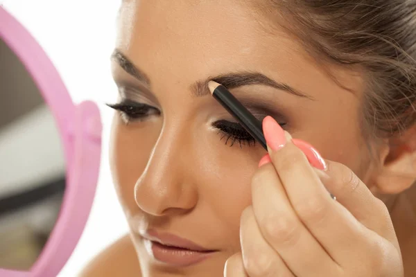 Young woman shaping her eyebrows with an eyebrow pencil