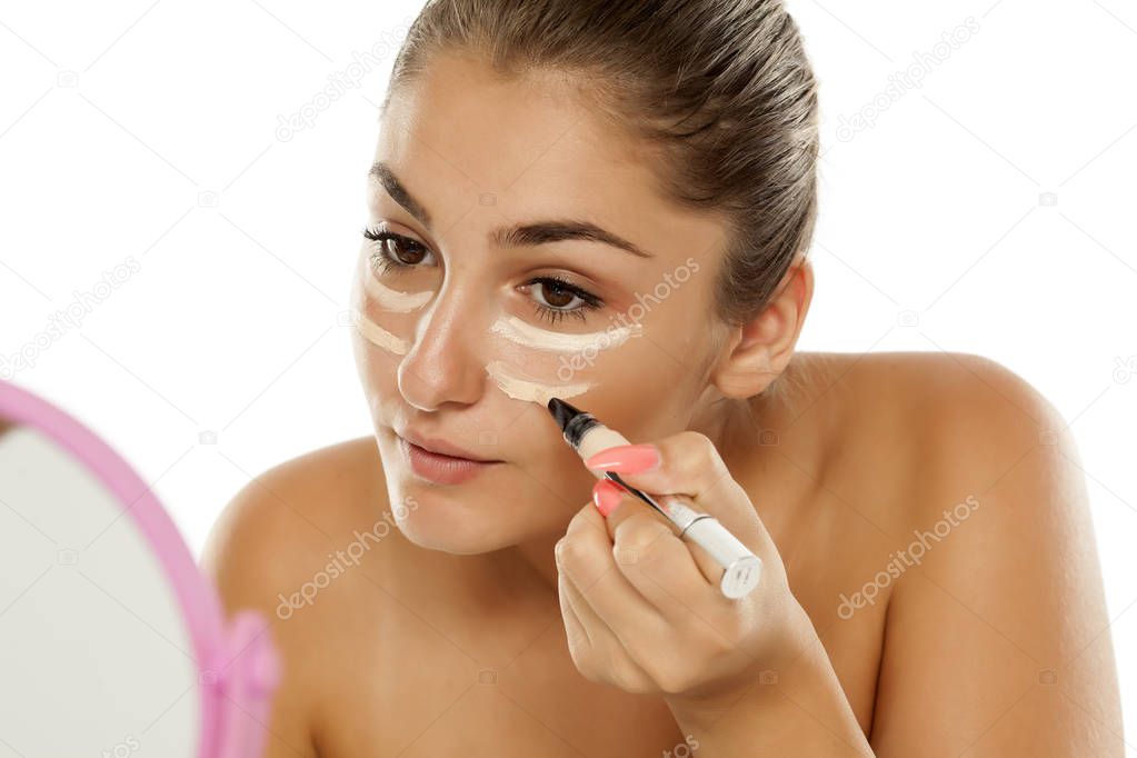 Young beautiful woman applying concealer under her eyes