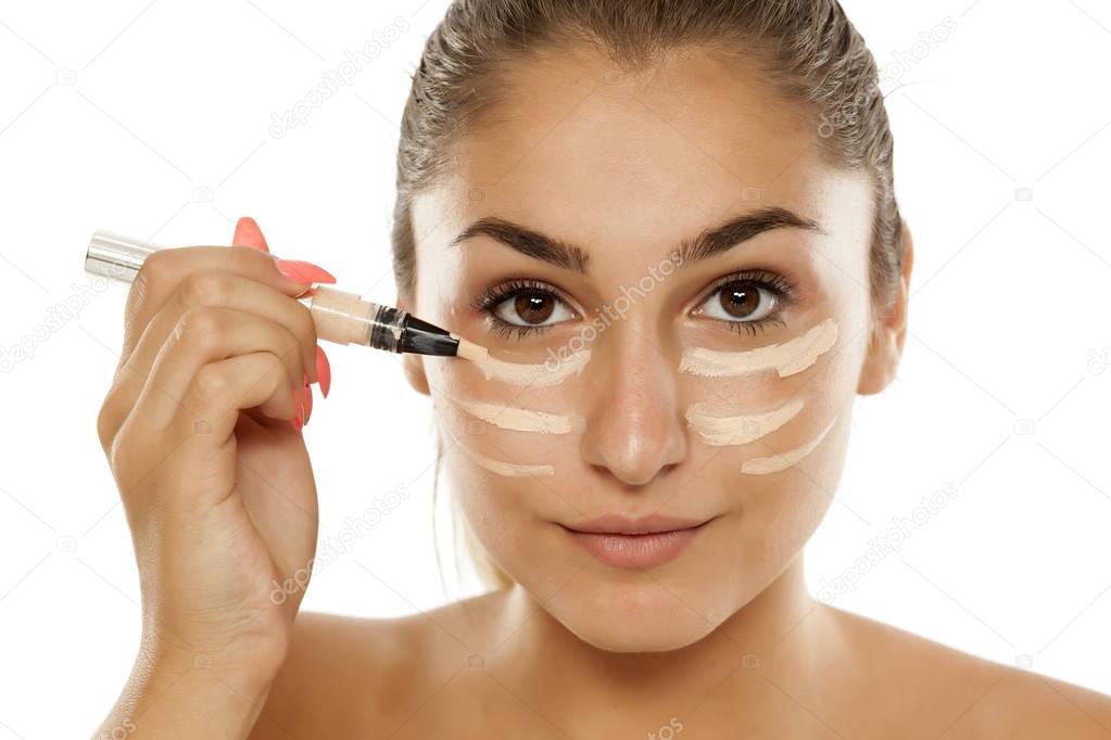 Young beautiful woman applying concealer under her eyes