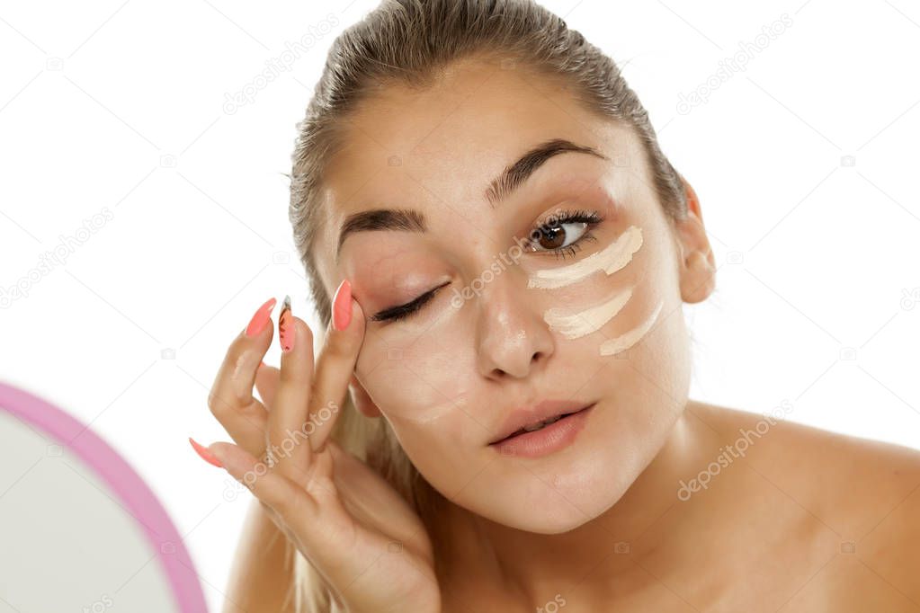 Young beautiful woman applying concealer under her eyes