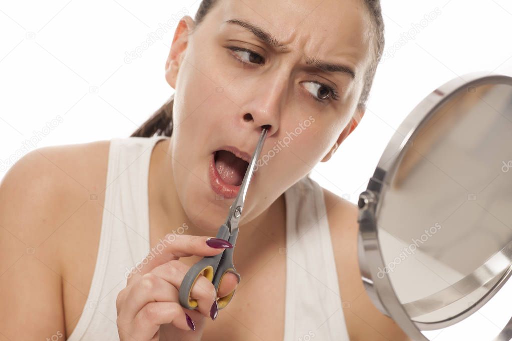 Young woman trimming the nose hair in the mirror