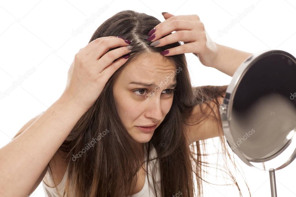 Young nervous woman looking at her hair and scalp in the mirror
