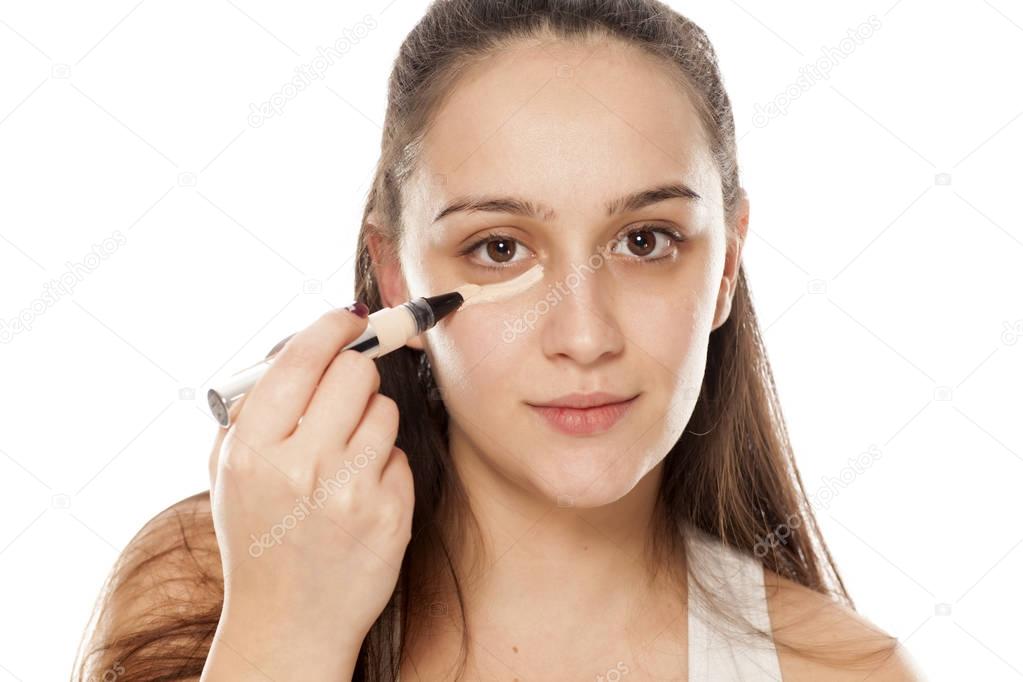 Young woman applying concealer under her eyes with a brush