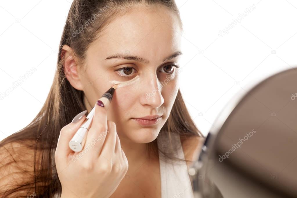 Young woman applying concealer under her eyes with a brush