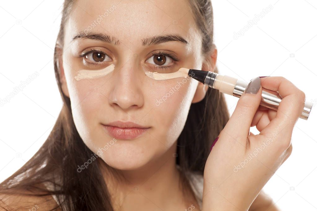 Young woman applying concealer under her eyes with a brush