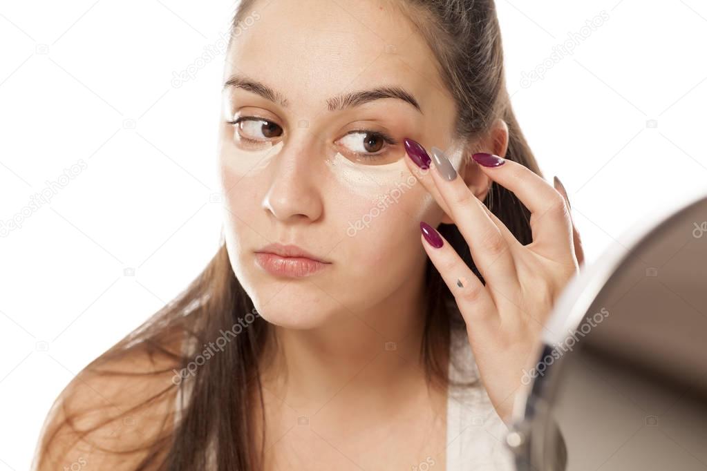 Young woman applying concealer under her eyes with her fingers