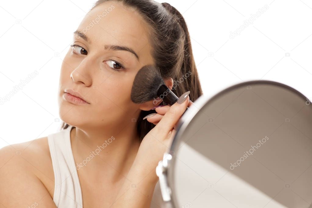 Young woman applying powder foundation on her face with a brush