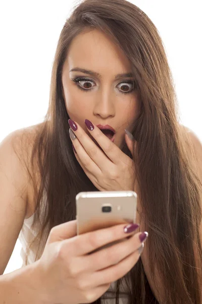 Mujer Joven Conmocionada Mirando Teléfono Inteligente Sobre Fondo Blanco — Foto de Stock
