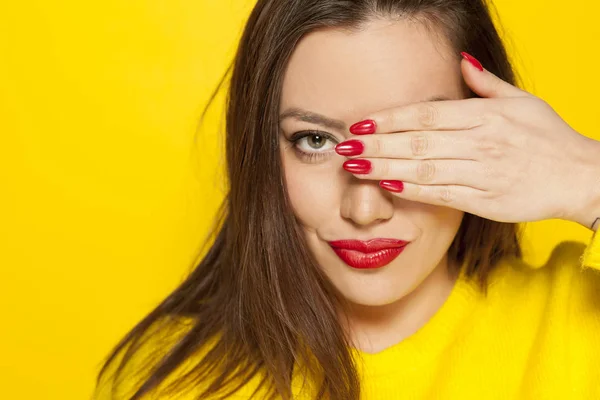 Beautiful woman in yellow blouse, covering her eye with her hand on a yellow background