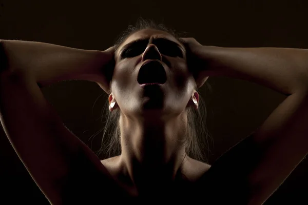 Woman in shadow screaming on a dark background