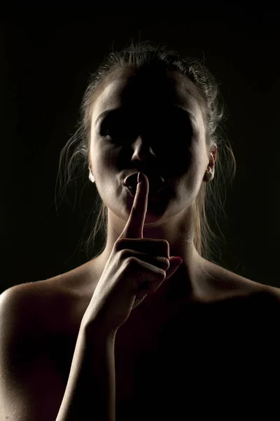 神秘的女人在阴影与她的手指在她的嘴唇在黑暗的背景 — 图库照片
