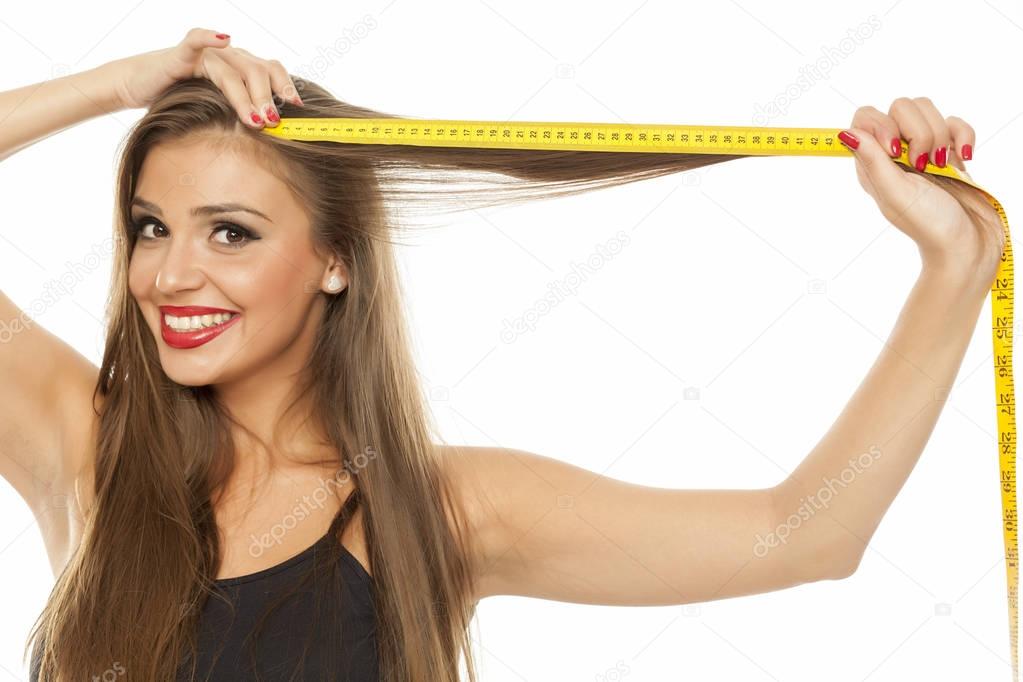 Happy young beautiful woman measuring her hair with a measuring tape