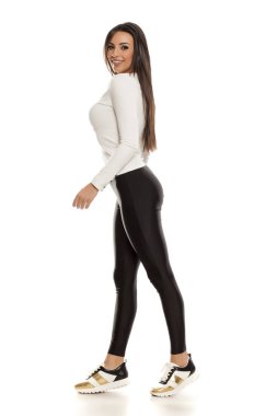 Beyaz bir arka plan üzerinde siyah tozluk, beyaz bluz ve spor ayakkabı güzel bir genç kadın yan görünüm