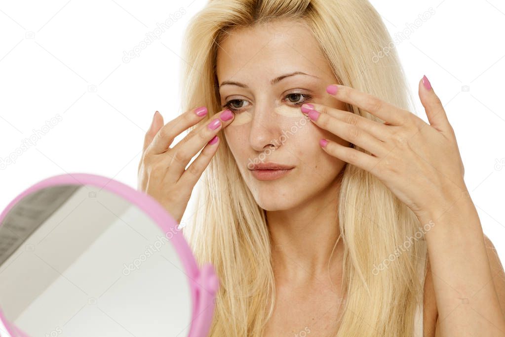 Young blonde woman applying concealer under her eyes