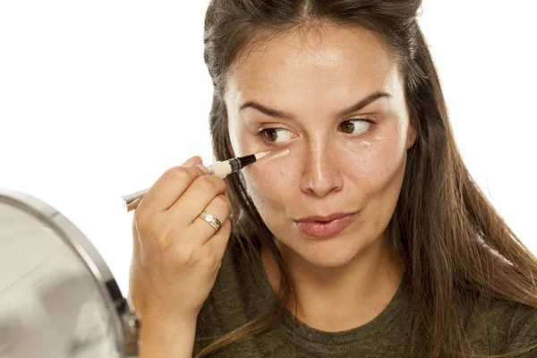 Mujer Joven Aplicando Corrector Bajo Sus Ojos Sobre Fondo Blanco —  Fotos de Stock