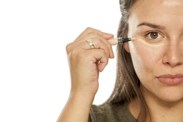 Mujer Joven Aplicando Corrector Bajo Sus Ojos Sobre Fondo Blanco —  Fotos de Stock