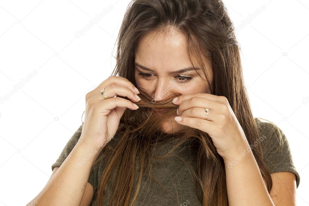 Nervous young woman smelling her hair on a white background