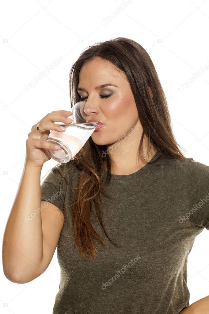 Young woman drinking water from a glass on a white background