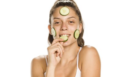 Beyaz arka planda yüzü salatalık dilimleriyle poz veren genç bir kadın. 