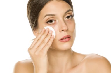 Genç ve güzel bir kadın beyaz arka planda pamukla yüzünü şıngırdatıyor.