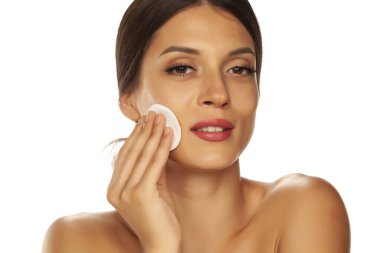 Genç ve güzel bir kadın yüzünü pamuklu bezle beyaza vuruyor. 