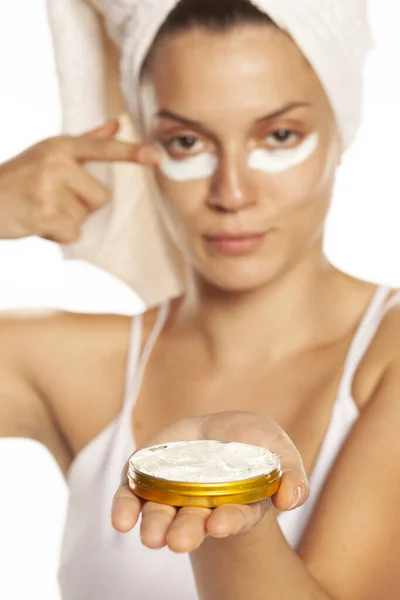 Mujer joven aplicando crema facial bajo sus ojos en el fondo blanco —  Fotos de Stock