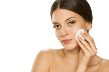 Genç ve güzel bir kadın beyaz arka planda pamukla yüzünü şıngırdatıyor. 