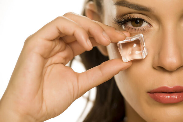 young beautiful woman holding ice cube under the eye on white background