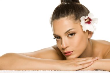 Saçında çiçek olan, beyaz bir arka planda yatan genç ve güzel bir kadının şehvetli portresi.