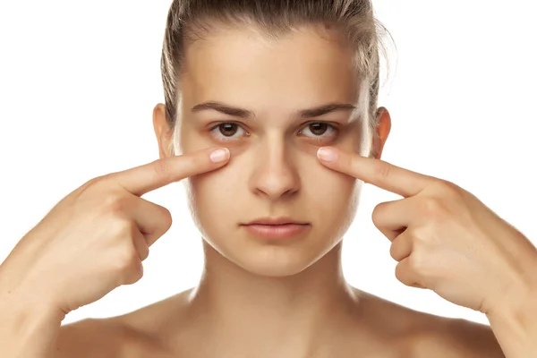 Junge Frau berührt ihre niedrigen Augenlider auf weißem Hintergrund — Stockfoto