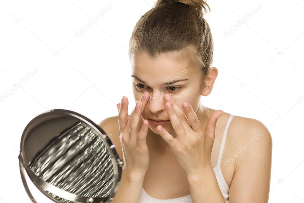 Portrait of young woman applying concealer with her fingers on white background