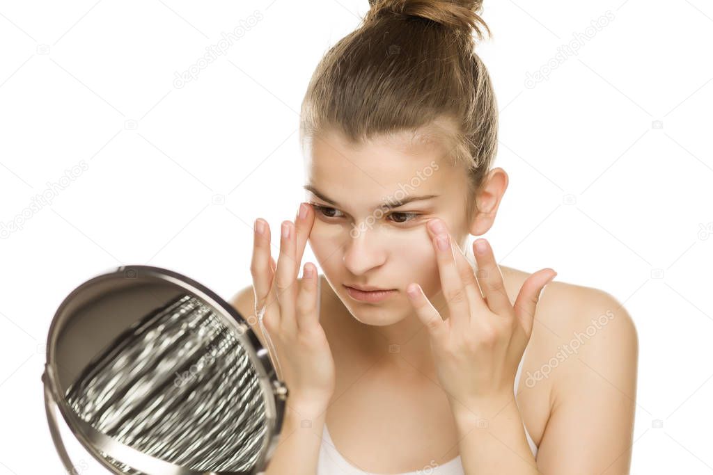 Portrait of young woman applying concealer with her fingers on white background