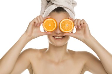 Kafasında havluyla genç ve güzel bir kadın beyaz arka planda gözünün önünde portakal dilimleri tutuyor.