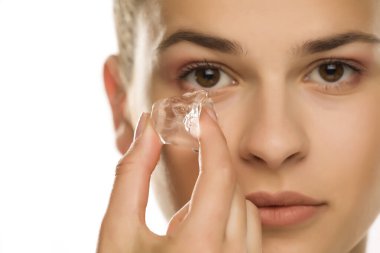 Beyaz arka planda, gözünün altında buz küpü tutan güzel bir kızın portresi.