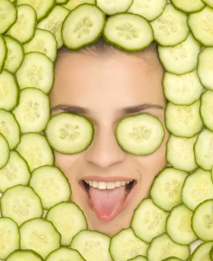 Young beautiful woman posing with slices of cucumber around her face clipart