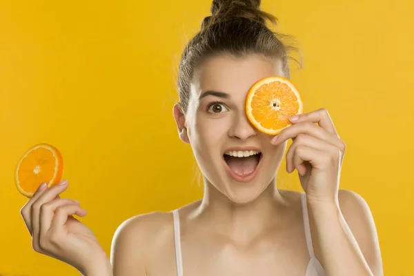 Молода Красива Жінка Тримає Шматочок Апельсина Перед Очима Жовтому Тлі — стокове фото