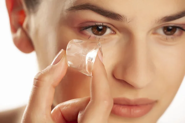 Retrato de joven hermosa sosteniendo el cubo de hielo bajo su ojo en wh —  Fotos de Stock