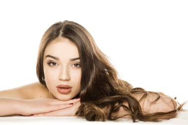 Makyajlı, uzun saçlı, beyaz arka planda yatan genç bir kadın.