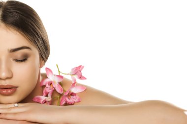 Makyajlı, beyaz arka planda orkidelerle poz veren genç kadın portresi.