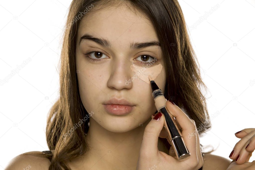 Young beautiful woman applying concealer on white background