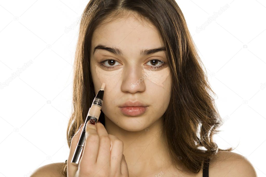 Young beautiful woman applying concealer on white background