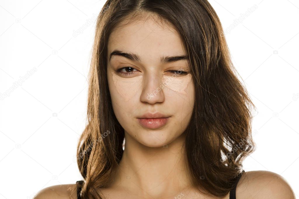 Young beautiful woman with concealer, winking on white background