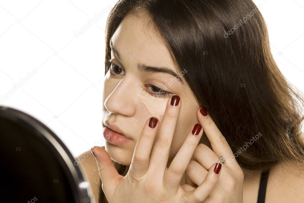 Young beautiful woman applying concealer with the fingers on white background